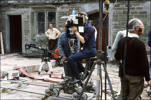 Survivors' crew members prepare to record a scene from Something of Value, with the OB camera mounted on a tracked dolly, in the inner courtyard of Hampton Court, some time between 5-9 June 1975. The breeze-block 'dam' is still in construction at this point in the shoot.